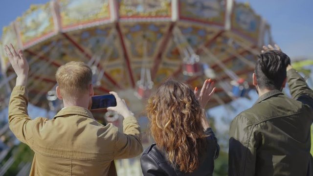 Three young parents wave to and take photos of their children riding carousel