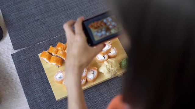 Girl takes pictures of sushi on phone. A girl takes pictures of sushi on the phone that lie on a black wooden table.