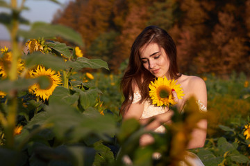 Beautiful lovely girl enjoying nature on a field of sunflowers. Sunlight plays on the field. Autumn time.