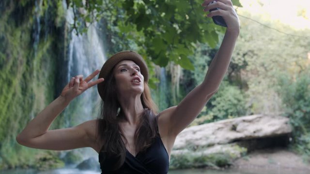 Woman taking selfie using phone near waterfall at national park happy smiling enjoying nature and lifestyle on vacation.