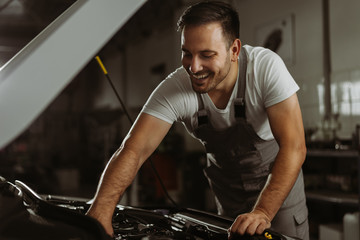 Fototapeta na wymiar Young smiling auto mechanic examining engine in a workshop
