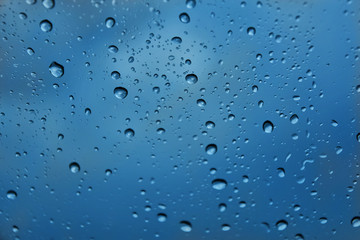 Rain drops with selective focus on transparent glass. Glass surface with water drops, blue toned. Window with raindrops. water drops on glass