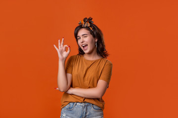 Smiling brunette woman in an orange t-shirt and beautiful headband showing OK-sign with fingers and...