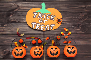 Text Trick or Treat with pumpkin buckets and candies on wooden background