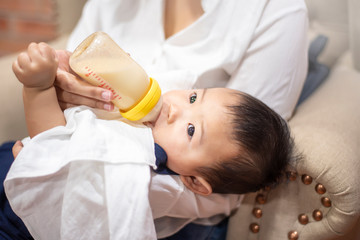 Obraz na płótnie Canvas Newborn cute baby is drinking milk from bottle by mom