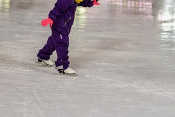 Small child in overalls learn to skate outdoors at the rink in the winter park