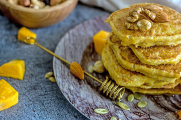 Pumpkin pancakes with honey, nuts and berries on a plate. Homemade pumpkin pancakes autumn food.  Pumpkin pancakes with maple syrup and honey on dark table. Pumpkin pastries for breakfast. 
