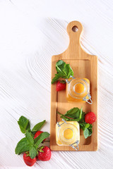 Honey in jars in assortment on a wooden board with strawberries on a white background. Still life concept. View from above. Macro photo.