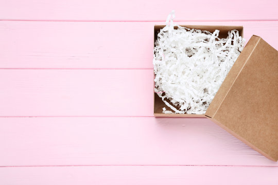 Open gift box with white shredded paper on pink wooden table