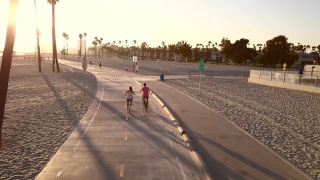 Sunset drone shot at the beach as two people ride off on bicycles
