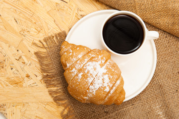 Croissant with a cup of coffee on a plate. Top view