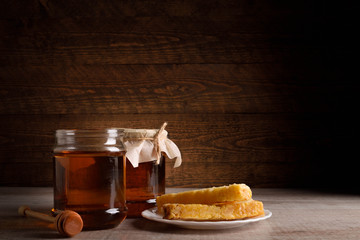 Honey in cans as well as honeycomb sots a wooden spoon on a wooden background