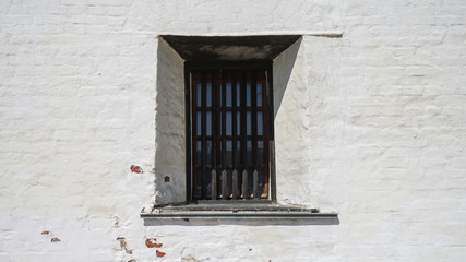 A small window with black bars on the background of a white brick wall.