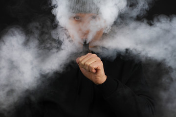 Men smoke an electronic cigarette on the dark background. Selective focus