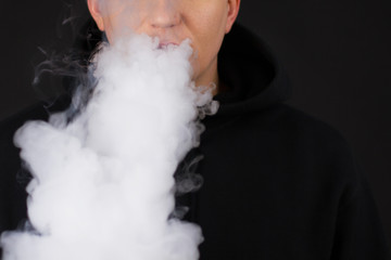 Vaping white man holding a mod. A cloud of vapor. Black background. Vaping an electronic cigarette...