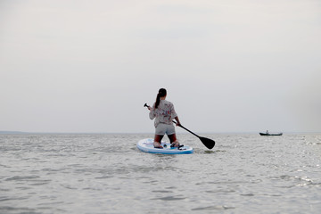 Fototapeta na wymiar Girl on sup board. Water sport, supsurfing. Active weekend at sea, woman leisure stand