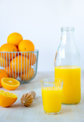 Glass and glass bottle with orange juice with fruit bowl full of fresh oranges