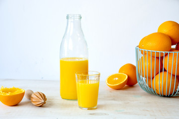Glass and glass bottle with orange juice with fruit bowl full of fresh oranges