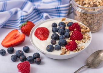 White yogurt in bowl with oatmeal and strawberries, blueberries and raspberries on the top.