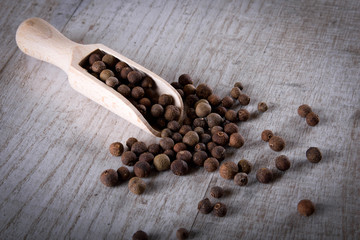 Pepper peas in a wooden spoon on a wooden background. Spices are scattered on the table