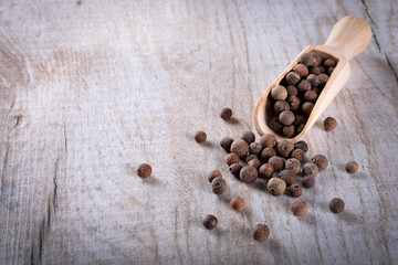 Pepper peas in a wooden spoon on a wooden background. Spices are scattered on the table