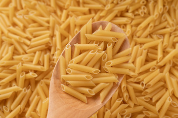 A wooden scoop scoops a bunch of wheat pasta