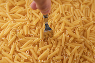 Man's hand sticks a shiny fork into a pile of wheat pasta