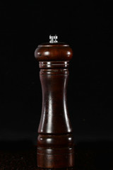 A device for grinding pepper or salt. Wooden mill on a black background. Still life concept. Copy...