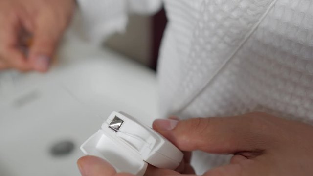 A man in a white Bathrobe opens a box of dental floss and takes it out. Oral hygiene