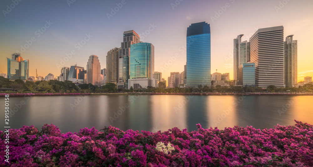 Wall mural lake with purple flowers in city park under skyscrapers at sunrise. benjakiti park in bangkok, thail