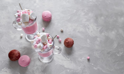 Pink hot chocolate with whipped cream and marshmallows. Macaroons on the grey background. Top view
