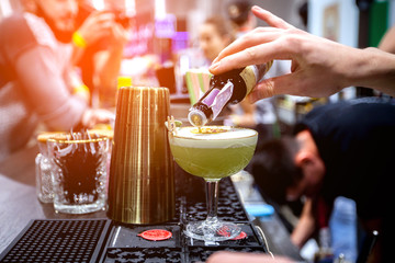 bartender is preparing an alcoholic cocktail in a glass glass, he is decorating the drink with flowers