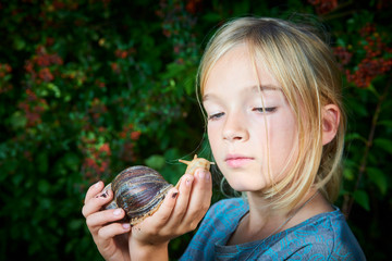Portrait of preteen adorable child girl playing with her pet giant African snail (Achatina fulica). Concept of not to be afraid of unusual animals. Selective focus