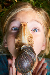 Portrait of preteen adorable child girl playing with her pet giant African snail. Snail crawling...