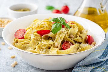 Fettuccine pasta with sauce pesto, cherry tomatoes, pine nuts and parmesan cheese on concrete...