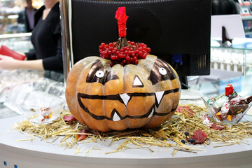 Orange big pumpkin with viburnum on top with a black marker drawing, white fangs, halloween in a shopping center close-up