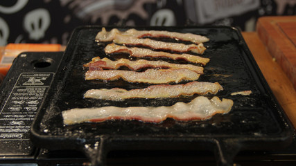 Bacon sizzling in the grill with shining fat bubbles