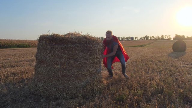 Cheerful father and son in superheroe roles running across wheat field while playing catch-up among straw stacks. Happy playful family having fun in nature while pretending to be superheroes