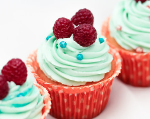 Tasty cupcakes with three large fresh raspberries on top