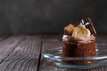  A biscuit cake is sprinkled with cocoa with chocolate cream, a heart of white chocolate, a slice of chocolate tile  and a delicious waffle on wooden background.