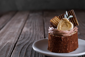  A biscuit cake is sprinkled with cocoa with chocolate cream, a heart of white chocolate, a slice of chocolate tile  and a delicious waffle on wooden background.