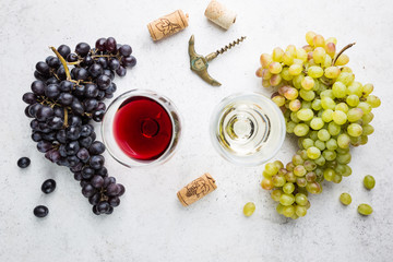 Glasses of white and red wine with ripe grapes on stone background, top view
