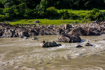 stream of the river Ganges with rocks on the shore and a green forest near Rishikesh, Uttarakhand,...