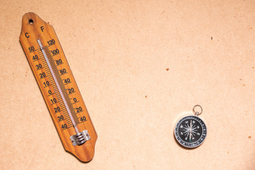 Temperature termometer and compass on wooden table.