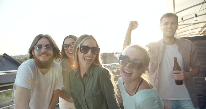 Group of happy stylish youth dancing on rooftop party and smiling to camera, enjoying good time