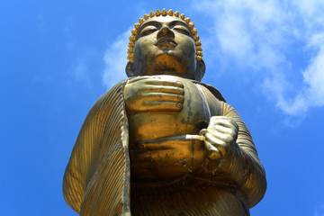 Obraz premium Golden statue of a standing Buddha against a blue sky