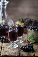 homemade black chokeberry wine or liqueur with ripe berries on wooden background