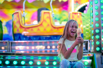 Smiling girl eating ice cream in the park of Funfair lights carnival
