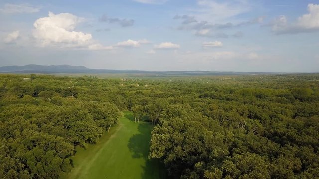 golf course in a forest of ash with the historic monastery of escorial crowning a hill, aerial view over a golf fairway
