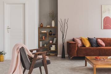 Grey vintage armchair with pastel pink blanket in elegant and atmospheric apartment